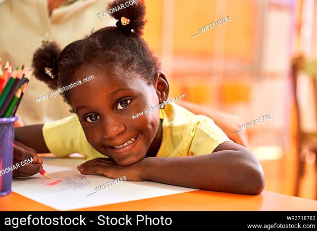 Fröhliches Mädchen mit Zöpfen malt ein buntes Bild mit Buntstiften im Malkurs der Grundschule