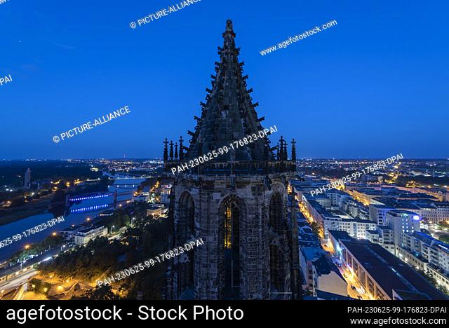 25 June 2023, Saxony-Anhalt, Magdeburg: The south tower of Magdeburg Cathedral towers over the state capital. The illuminated lift bridge can be seen on the...