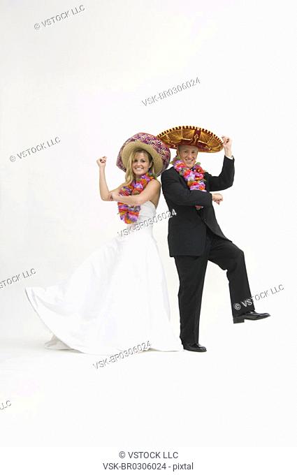 Bride and groom wearing sombreros and flower leis while dancing