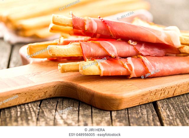 Parma ham prosciutto with grissini breadsticks on cutting board
