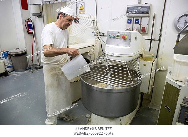 Baker pouring water in an industrial kneading machine