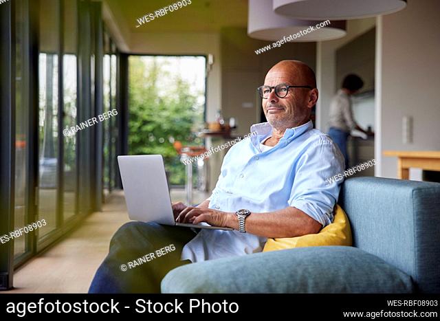 Thoughtful man with laptop sitting on sofa at home