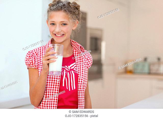 Smiling girl with milk mustache holding glass of milk