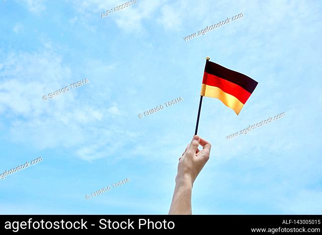 Hand holding flag against blue sky