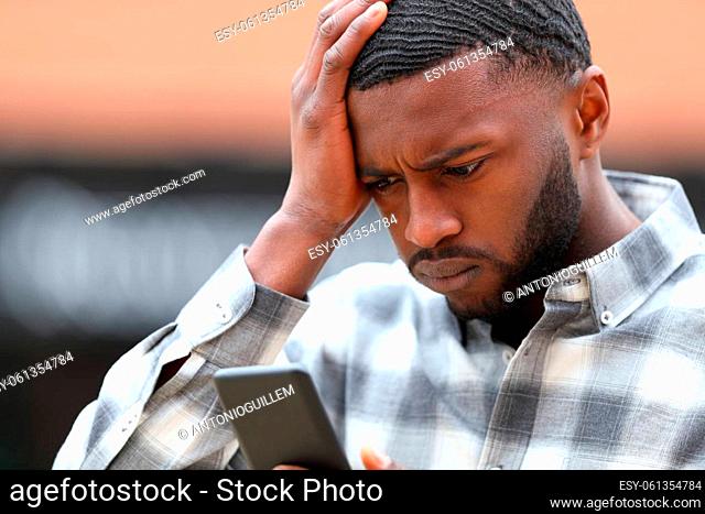 Worried man with black skin complaining checking smart phone content in the street