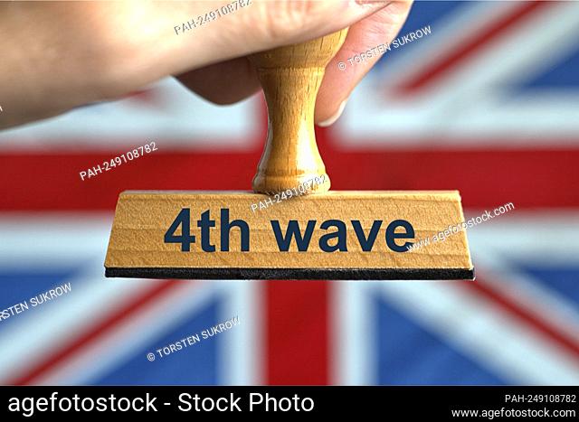 A symbolic wooden stamp with the inscription ""4th wave"", held by a hand in a bleed in front of a blurred flag of Great Britain (GB)