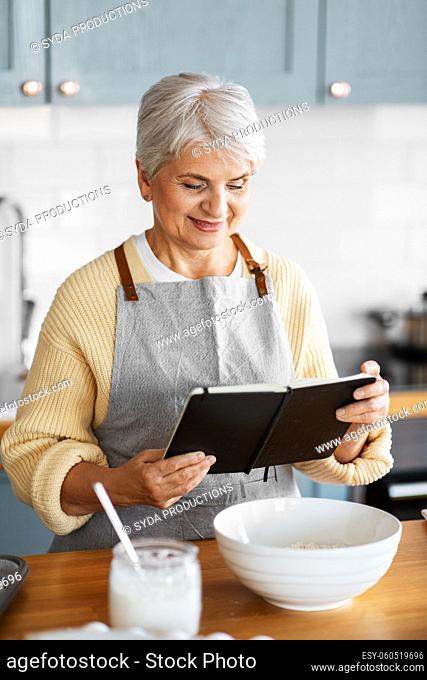 happy woman with cook book cooking food on kitchen