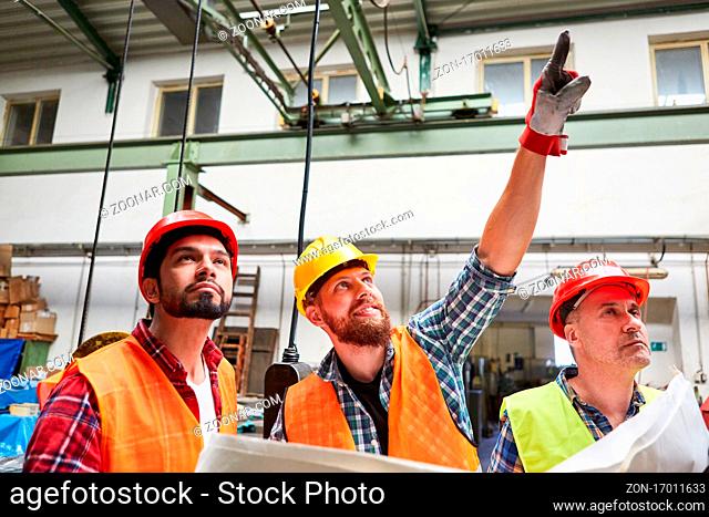 Handwerker und Bauarbeiter diskutieren mit Bauplan die Sanierung der Metallfabrik