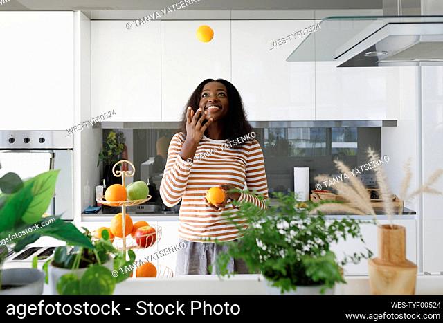 Happy woman juggling oranges in kitchen