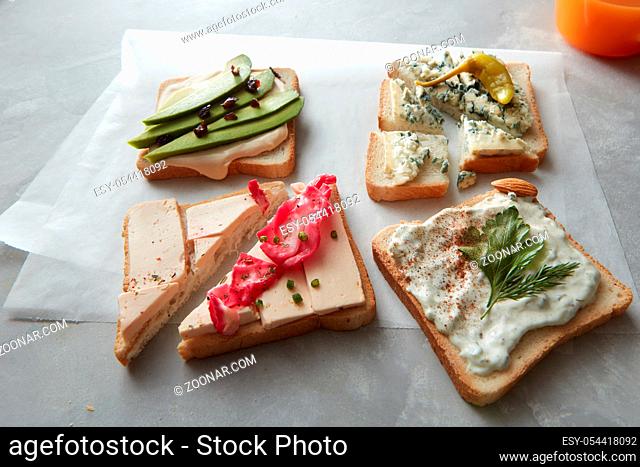 Food concept. Snack concept. Different kinds of colorful sandwiches with rare ingredients and glass of orange juice for having snack or break over white cooking...