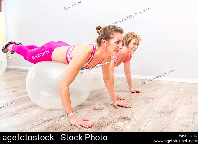 Two young smiling women lying on transparent pilates ball