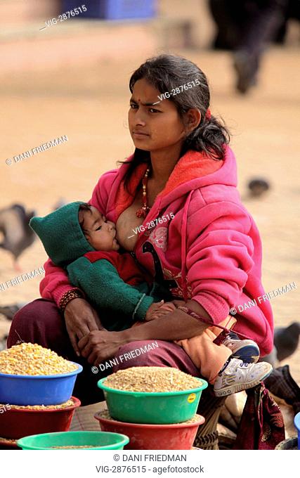 NEPAL, KATHMANDU CITY, 06.12.2011, A young woman selling seed for pigeons feed takes a break to breastfeed her child at the base of the Bodhnath Stupa in...