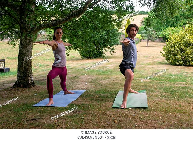 Man and woman doing yoga in garden, practicing warrior pose