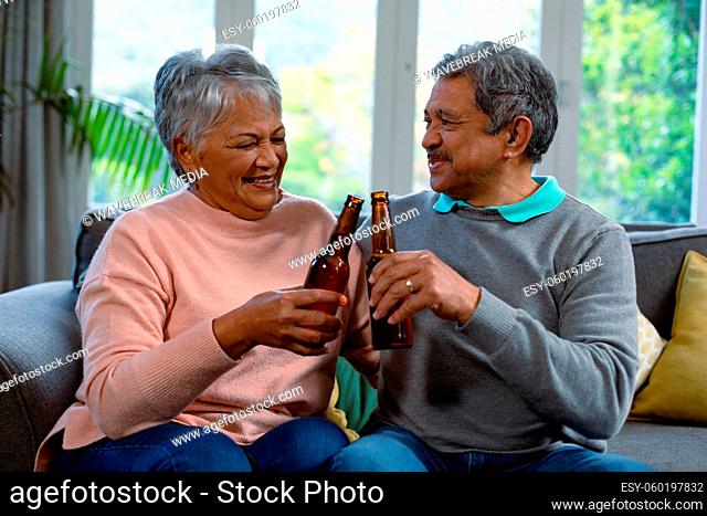 Happy diverse senior couple sitting on sofa and drinking beer