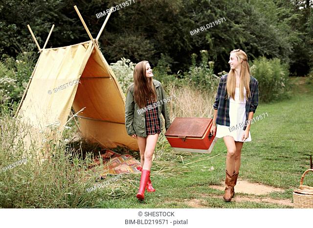 Women carrying vintage cooler near camping tent in forest