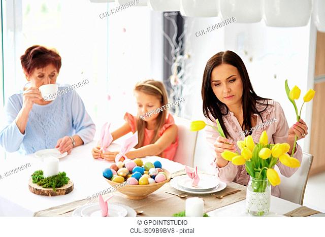 Woman with daughter and mother arranging yellow tulips at easter dining table