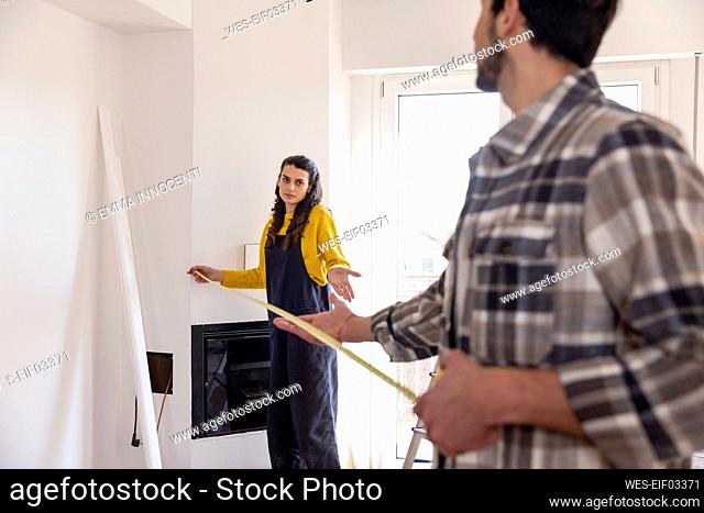 Confused woman with measuring tape talking with boyfriend in new living room