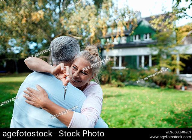 Smiling woman with house key hugging man at backyard