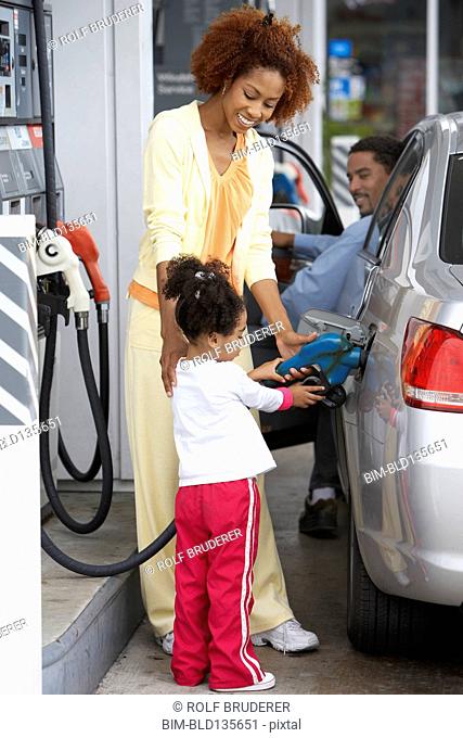 Black mother teaching daughter to pump gas