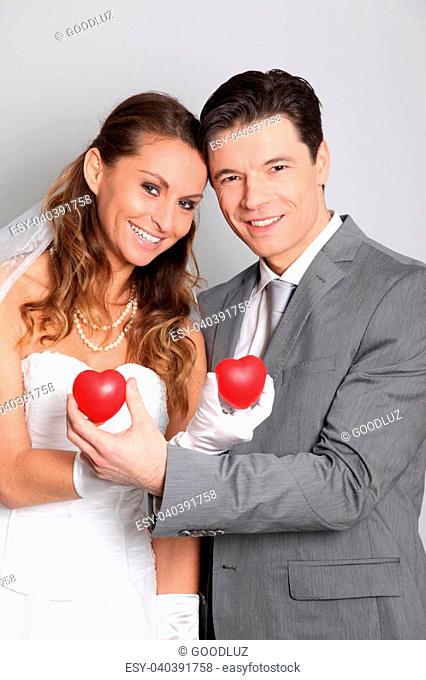 Bride and groom holding red hearts on white background