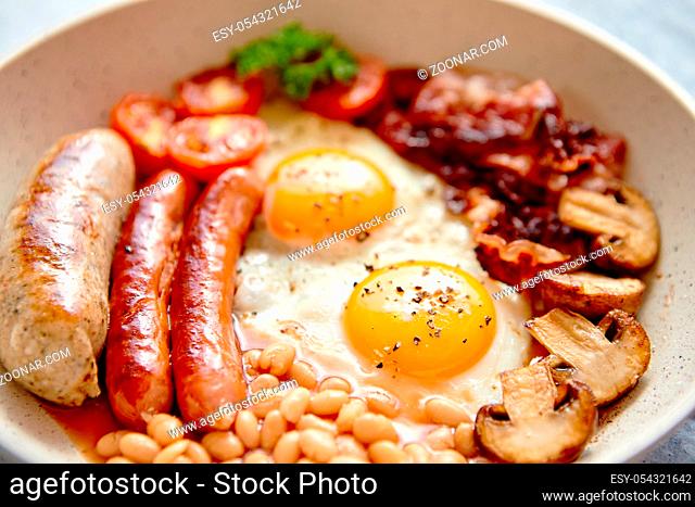 British Full English Breakfast including sausages, grilled tomatoes, mushrooms, eggs, bacon, baked beans and bread. Top view