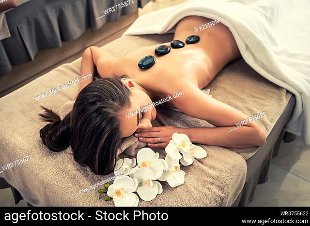 High angle view of young woman lying down on massage bed with traditional hot stones along the spine at spa and wellness center