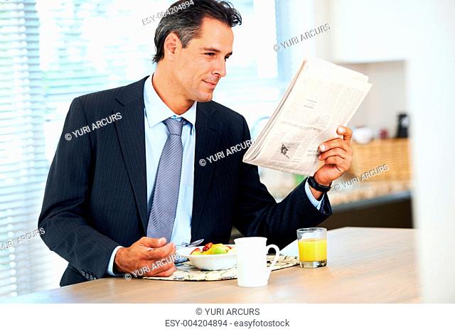 Handsome businessman reading the morning paper and enjoying a healthy breakfast