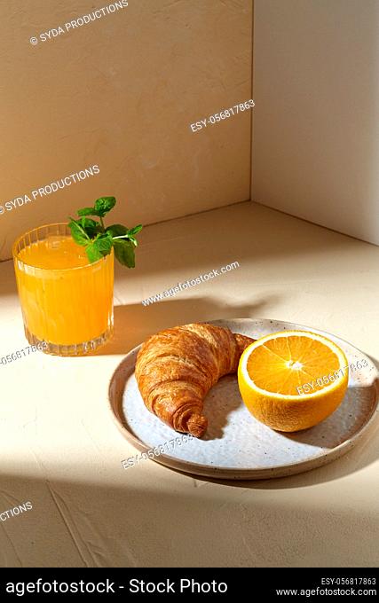 glass of orange juice and croissant on plate