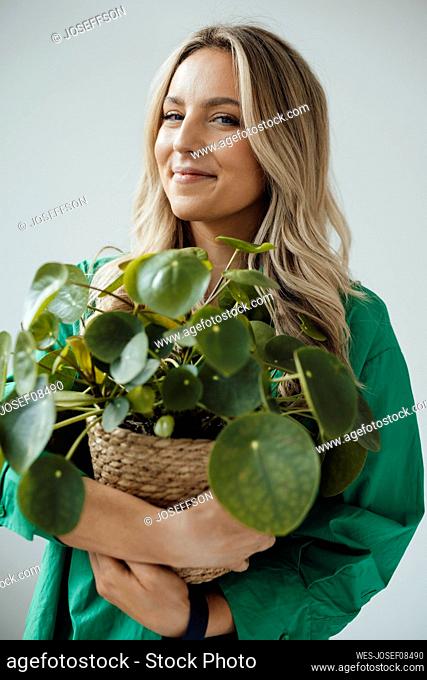 Smiling woman holding houseplant standing against white background