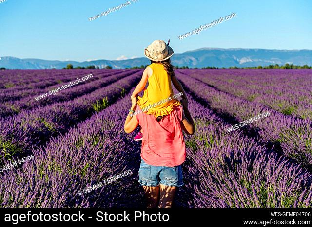 Mother piggybacking little daughter in vast summer lavender field