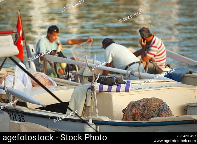 Fishermen mending nets on a traditional fishing boat inside the harbour of Kas village in the afternoon light, Antalya Province, Mediterranean Coast