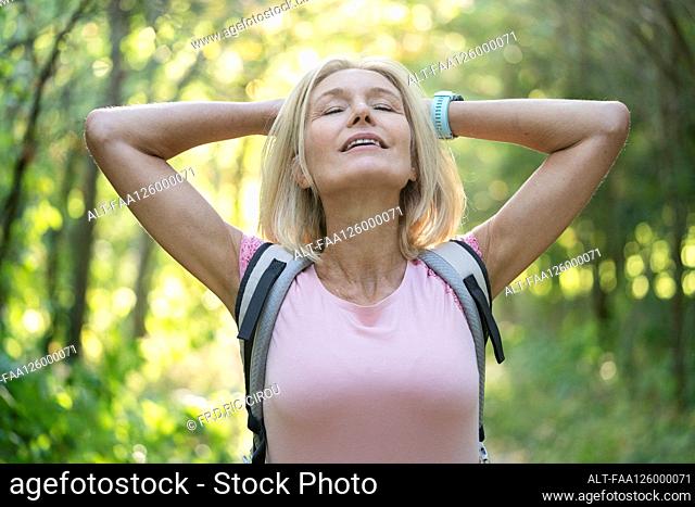 Mature woman with hands behind head standing in forest