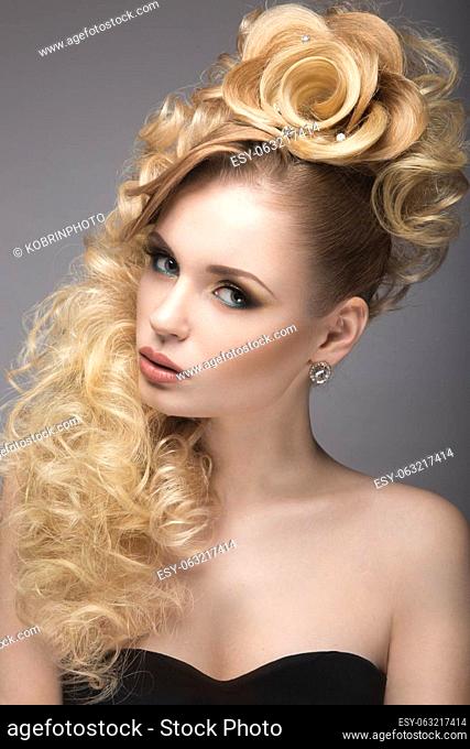 Beautiful blonde girl in evening dress with an unusual hairstyle in the form of roses and bright makeup. Beauty face. Picture taken in the studio on a gray...