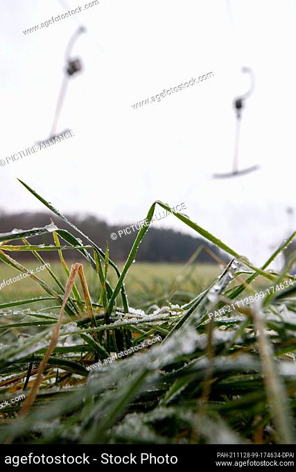 28 November 2021, Saxony, Rugiswalde: A little bit of snow lies in the grass under the abandoned and icy lift in the ski resort in Saxon Switzerland on the...