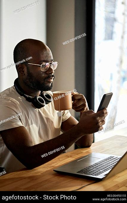 Man using smart phone holding tea cup sitting at home