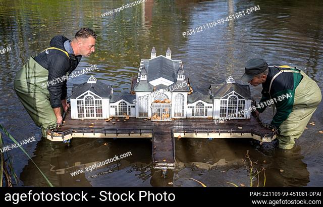 09 November 2022, Saxony, Lichtenstein: André Döhn (l) and Johannes Dengis, employees at Miniwelt in Lichtenstein, lift a model of the Sellin pier out of the...