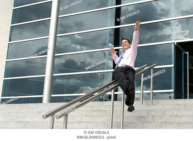 Hispanic businessman sliding down railing