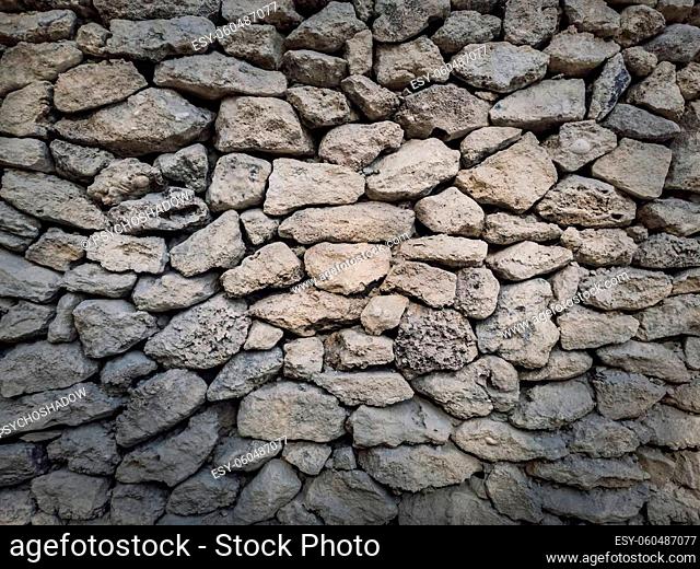 Irregular stone masonry wall background. Old limestone rocks of different size and shapes stacked carefully. Detailed texture of construction element