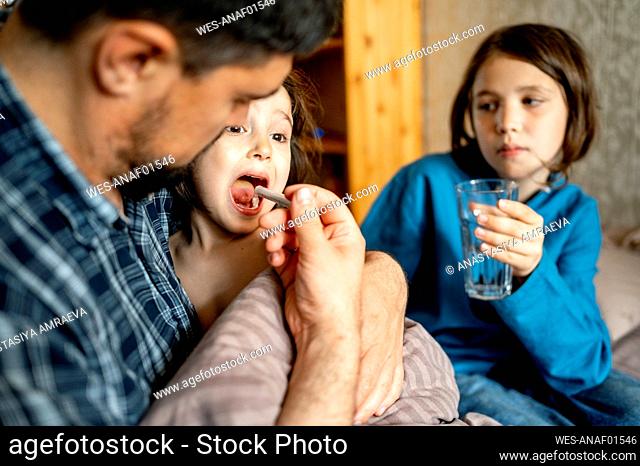 Father giving medicine to sick son at home