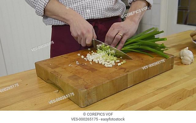 home chef cutting spring unions with a kitchen knife on a wooden cutting board
