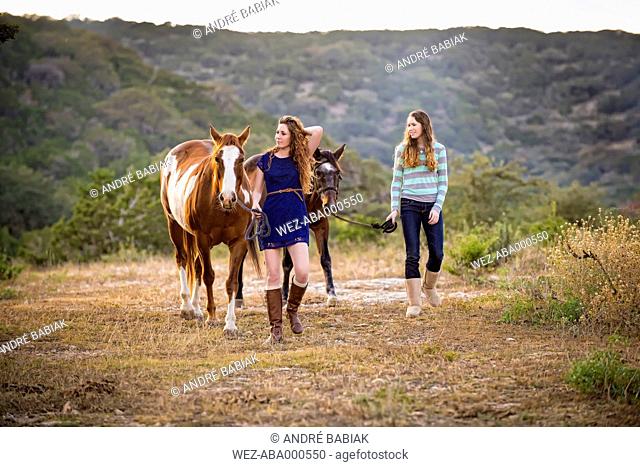 USA, Texas, Sisters walking with Quarterhorses near mountain