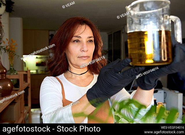 Woman measuring olive oil in beaker while making soap in workshop