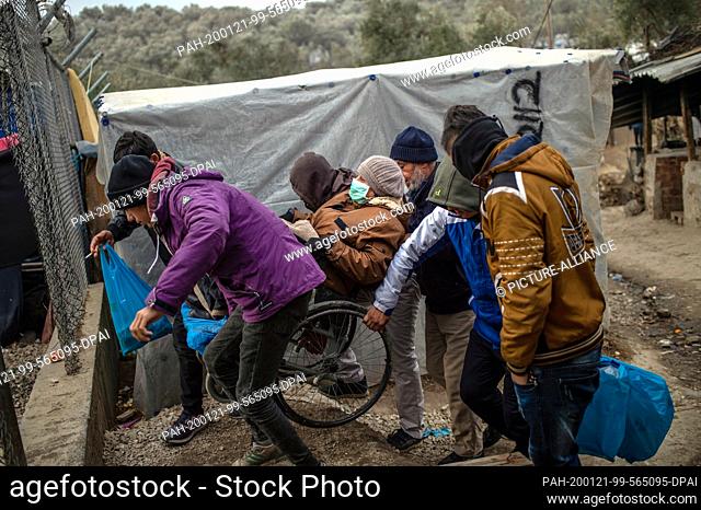 21 January 2020, Greece, Lesbos: Migrants carry a sick woman sitting on a chair in a temporary camp next to the camp in Moria
