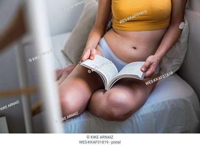 Close-up of young woman in underwear reading a book at home