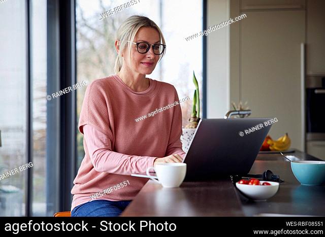 Blond woman using laptop in kitchen at home
