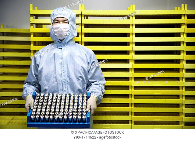 An employee of a battery company wearing a anti-contamination suit holding a crate of battery cells in front of a wall of crates