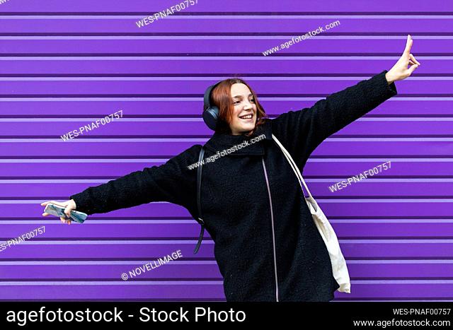 Cheerful young businesswoman dancing against purple shutter while listening music