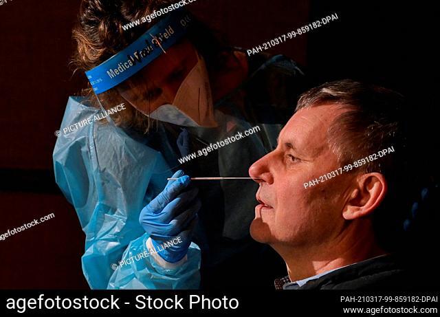 17 March 2021, Brandenburg, Kleinmachnow: Nurse Waltraud Friese pushes a cotton swab into the left nostril of Kleinmachnow's mayor Michael Grubert (SPD) during...