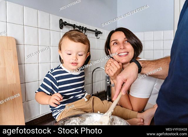 Excited mother with son looking at husband preparing food in kitchen at home