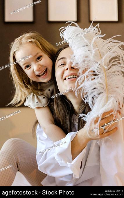 Happy mother and daughter playing with feather at home